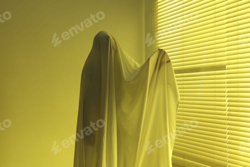 Preview: Creepy ghost. Man covered with white sheet indoors in yellow light