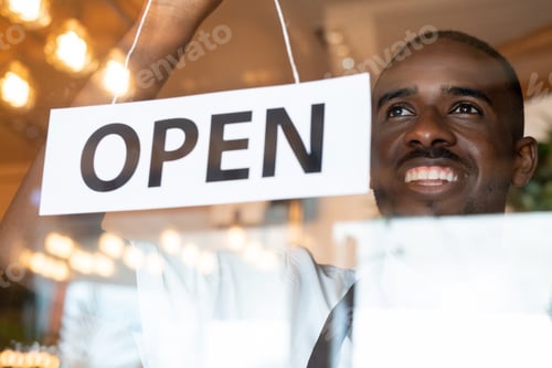 Preview: Happy young cafe worker hanging paper with notice open on transparent door