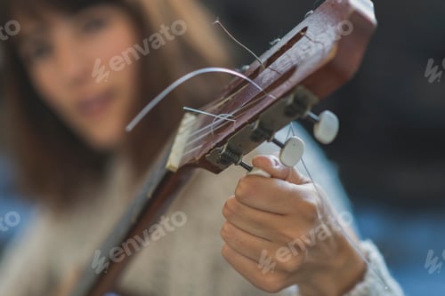 Preview: Beautiful young woman sitting on sofa playing guitar