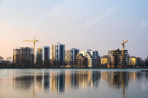 Preview: Tower cranes and high residential apartment buildings under construction on lake shore. Real estate