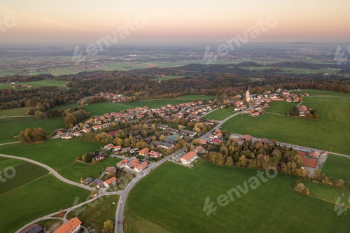 Preview: Aerial view of small town with red tiled roofs among green farm fields and distant forest in summer.