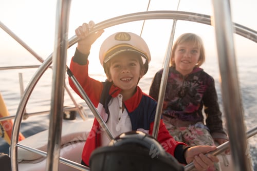 Preview: Smiling children holding steering wheel on yacht on water