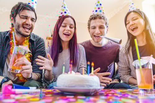 Preview: Group of happy friends celebrating birthday at home with cake and cocktails