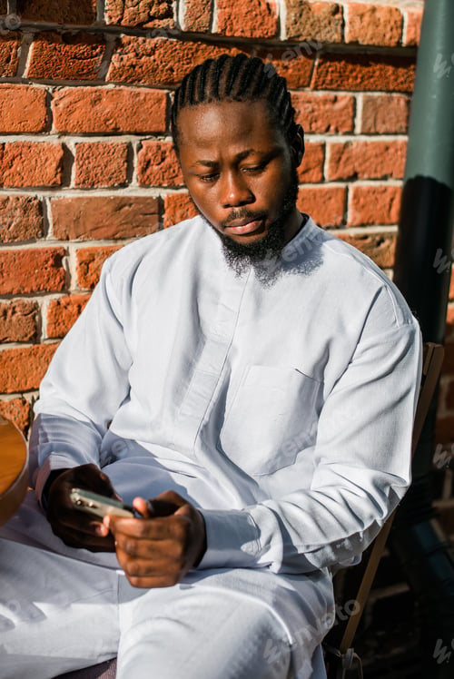 Preview: African american man in stylish ethnic dashiki wear viewing photos in social networks on mobile