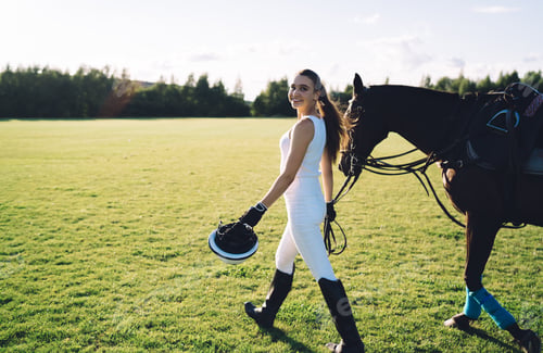 Preview: Female rider walking across green meadow with horse