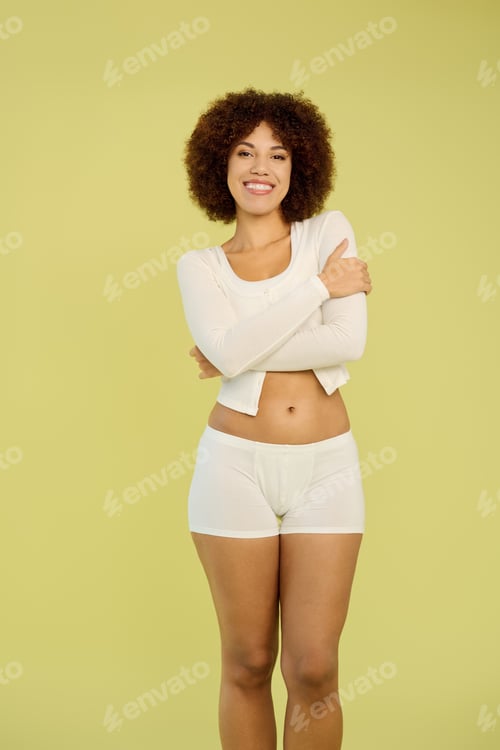 Preview: Joyful young Black woman with curly hair stands in underwear against a yellow backdrop