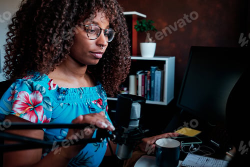 Preview: Woman using a microphone and computer while broadcasting a podcast from home.
