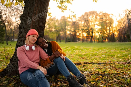 Preview: Diverse women friends relaxing under tree in autumn park