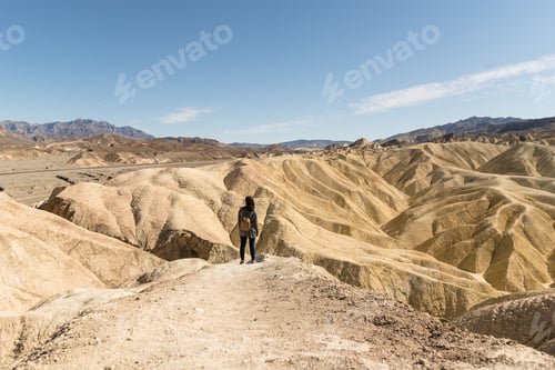Preview: Female with a backpack standing on the top of the hill under a blue clear sky