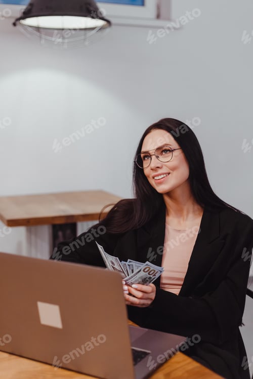 Preview: Woman Holding Money by Laptop in Bright Workplace