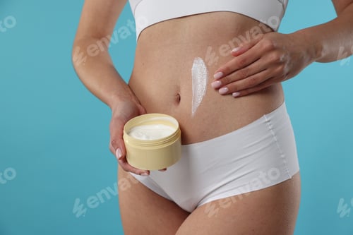 Preview: Woman applying anti cellulite cream on light blue background, closeup