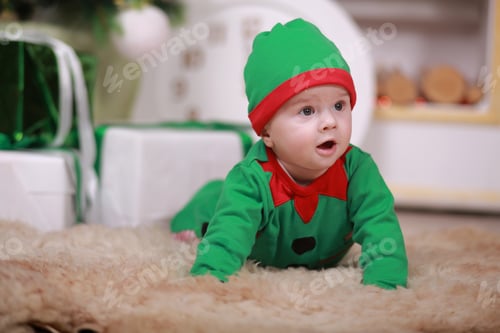 Preview: baby boy in red green elf costume sitting under Christmas tree and gift boxes