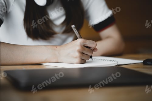 Preview: Close-up of female student taking notes on a notebook, she is studying online at home, The concept o