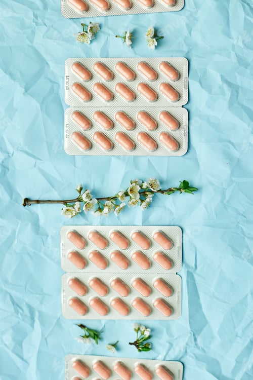 Preview: Pink Pills Arranged Neatly With White Blossoms on a Textured Blue Background