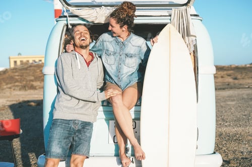 Preview: Happy surfers couple standing behind on vintage camper mini van
