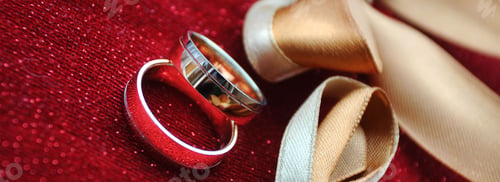 Preview: Two golden wedding rings on a red shiny pillow with a golden ribbon