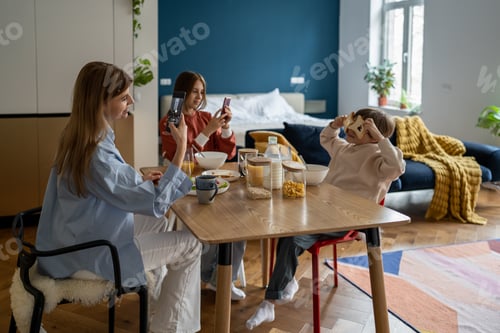Preview: Loving mom takes pictures on smartphone as son fooling around with bread toast at family breakfast