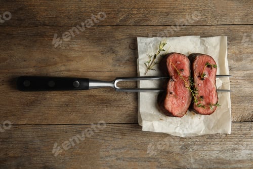 Preview: Fork with slices of meat on wooden table, top view