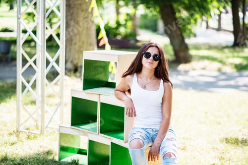 Preview: Portrait of a fashionably dressed girl posing on wooden boxes in the park on a sunny day