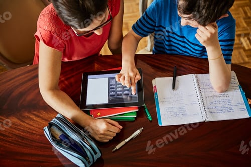 Preview: High angle view of mother at dining table helping son with homework