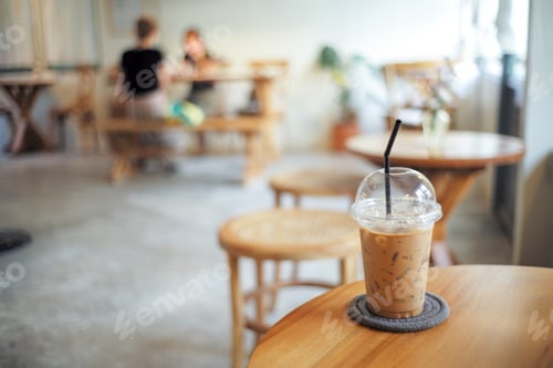 Preview: Ice coffee in the plastic glass on the wooden table at the coffee shop with people in background.