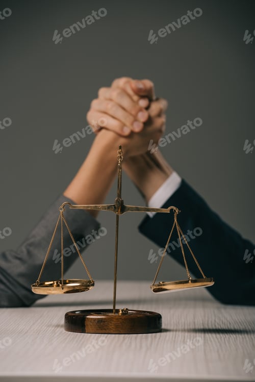 Preview: selective focus of business colleagues arm wretsling on wooden table with scales of justice on grey