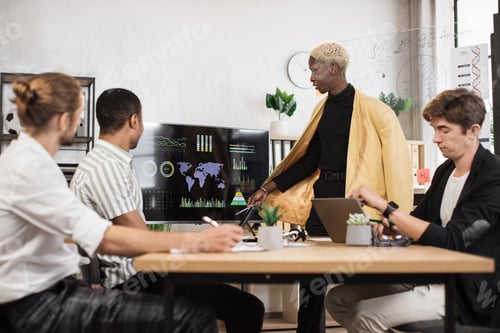 Preview: Group of four partners sitting at desk and listening speech of african american man near monitor