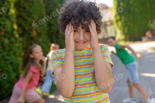Preview: Smiling boy covering face with palms and hiding friends
