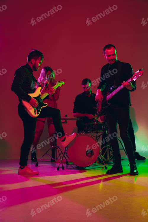 Preview: Young caucasian musicians, band performing in neon light on red studio background