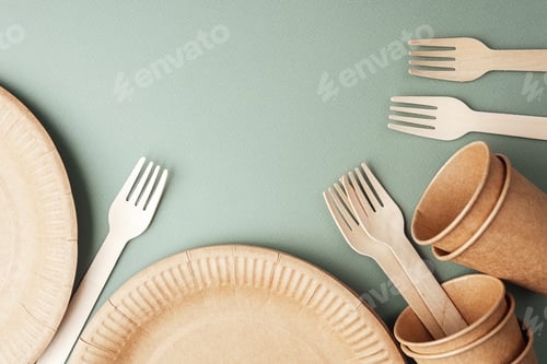 Preview: Disposable eco paper cups and wooden forks on green background flat lay view