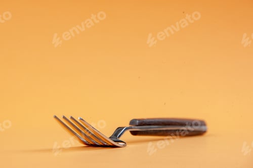 Preview: Above view of elegant metal fork on the bottom on golden background with free space