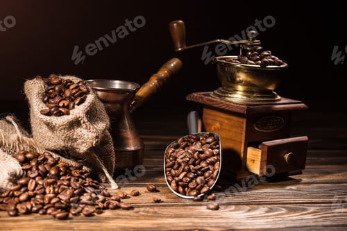Preview: metal scoop, vintage cezve and coffee grinder on rustic wooden table spilled with roasted beans