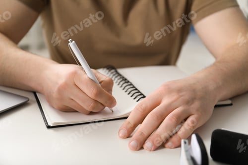 Preview: Man taking notes during online lesson at desk indoors, closeup. Self-study