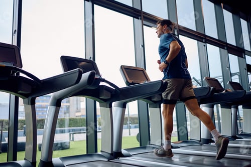 Preview: Athletic man running on treadmill during sports training at health club.