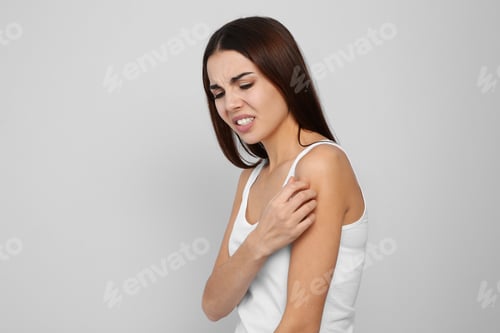 Preview: Young woman scratching shoulder on light background. Annoying itch