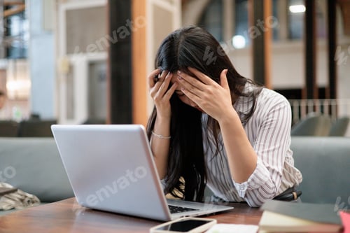 Preview: Stressed businesswoman holding head in hands while working on laptop