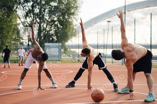 Preview: Three basketball players stretching on outdoor court before game