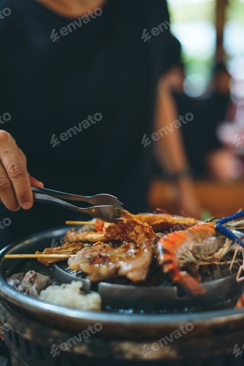 Preview: Close up Man is cooking and flipping grilled chiken, seafood meat with tong on traditional Asian BBQ
