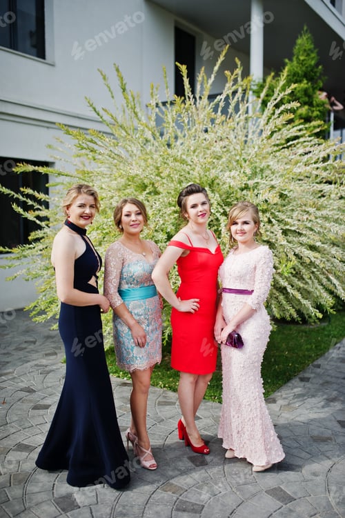 Preview: Faulous young women graduates in chic evening gowns posing outside in the park.