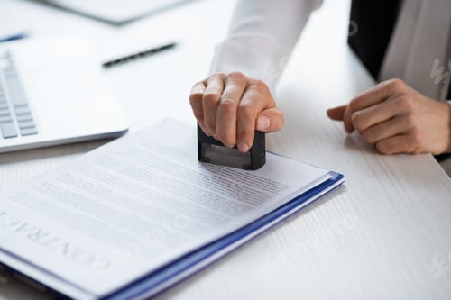 Preview: Close-up partial view of businesswoman stamping contract at workplace