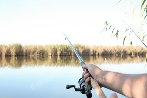 Preview: Man fishing alone at riverside on sunny day, closeup