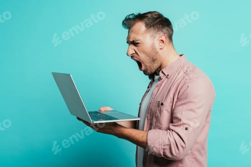 Preview: aggressive bearded man yelling at laptop, isolated on blue