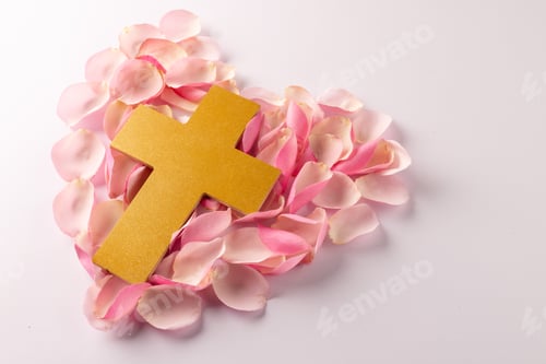 Preview: Overhead of yellow christian cross on heart shape of pink rose petals, on white with copy space
