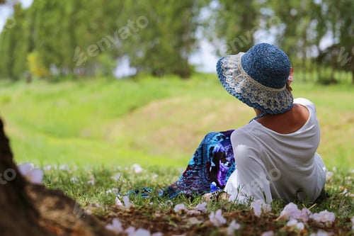 Preview: Woman with blue hat laying relax on green ground at outdoor park nature blur background