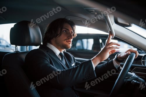 Preview: Young businessman in black suit and tie driving modern automobile