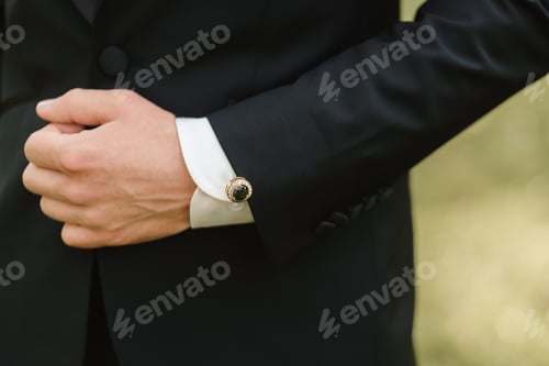 Preview: Elegant cufflink adorned suit hand positioned outdoors during a wedding celebration with