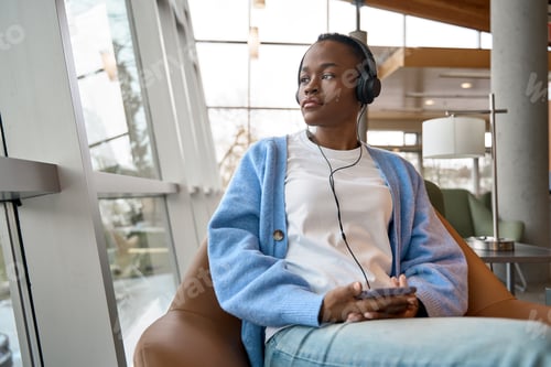 Preview: African Black girl student sitting in university campus wearing headphones.