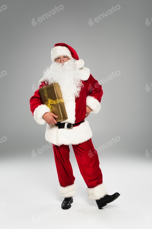 Preview: Full length of santa claus with present standing on grey background