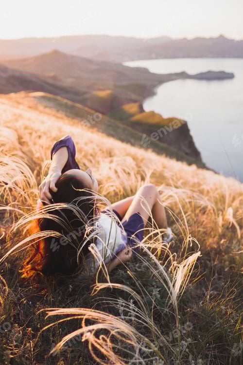 Preview: Young woman relaxing in feather grass field at sunset Enjoying beautiful mountain view and sea coast