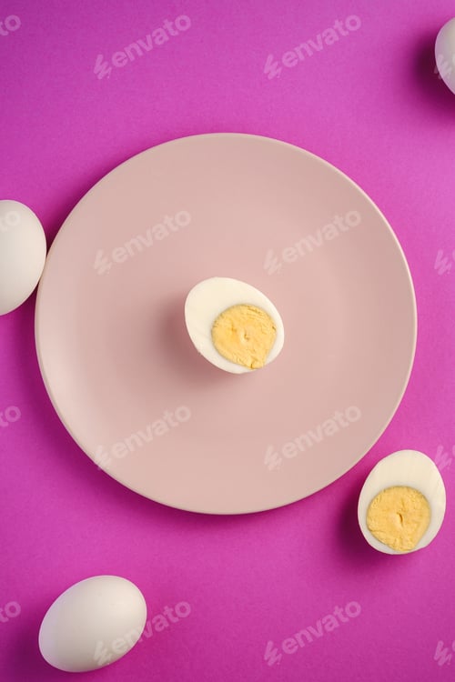 Preview: Boiled egg with yellow yolk in pink plate near to white eggs